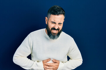 Young hispanic man wearing casual clothes with hand on stomach because nausea, painful disease feeling unwell. ache concept.