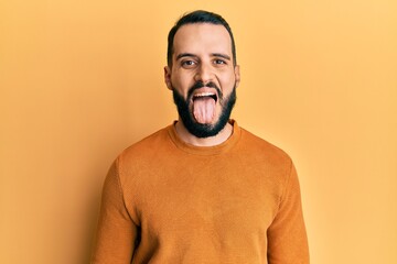 Young man with beard wearing casual winter sweater sticking tongue out happy with funny expression. emotion concept.