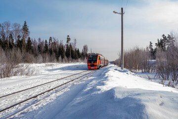 Red-orange train among white snow on a sunny winter day.