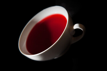 A white teacup with red berry tea. A black background