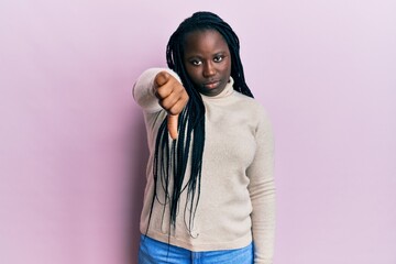 Fototapeta premium Young black woman with braids wearing casual winter sweater looking unhappy and angry showing rejection and negative with thumbs down gesture. bad expression.