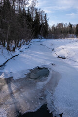 Winter landscape with a small snow-covered river on a sunny day.