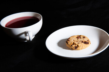 White cup of berry tea and cookie on the white plate. Black background