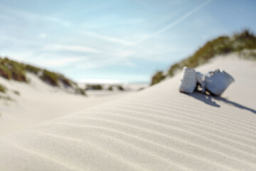 Against sunshine view on pair of white ankle sneakers laying on sand dune. North sea coastal landscape.