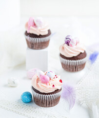 Three Easter chocolate cupcakes with caramel filling and decoration of small Easter eggs from marzipan on the white background. Selective focus