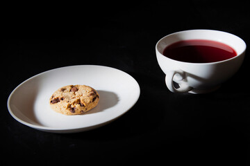 White cup of berry tea and cookie on the white plate. Black background