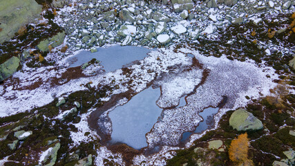 Mountain lake shore starting to freeze in autumn with amazing holes in the ice