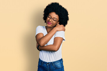 Young african american woman wearing casual white t shirt hugging oneself happy and positive, smiling confident. self love and self care