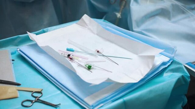 Used medical equipment - needles and catheters lie on a napkin on the medical table in the operating room and next to them are steel scissors and a clamp. Surgery.