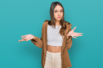 Young brunette woman wearing casual clothes clueless and confused expression with arms and hands...