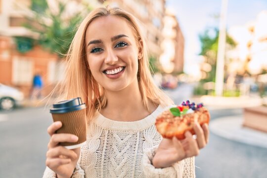 Young blonde girl smiling happy having breakfast standing at the city.