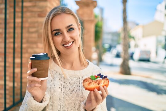 Young blonde girl smiling happy having breakfast standing at the city.