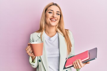 Young caucasian woman drinking a cup of coffee and holding laptop smiling with a happy and cool smile on face. showing teeth.