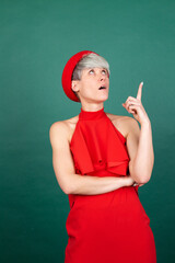 Studio portrait of stylish woman in red dress on green background stands serious point finger up