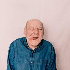 an elderly old man grimaces, makes a face and shows his tongue on a light background. crazy man