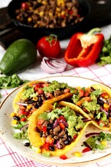 Mexican tacos with roast minced meat with corn and black beans, onions, fresh tomatoes, paprika and cilantro are flavored with guacamole sauce.