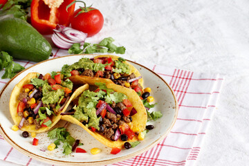 Mexican tacos with roast minced meat with corn and black beans, onions, fresh tomatoes, paprika and cilantro are flavored with guacamole sauce.
