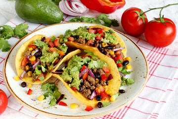 Mexican tacos with roast minced meat with corn and black beans, onions, fresh tomatoes, paprika and cilantro are flavored with guacamole sauce.