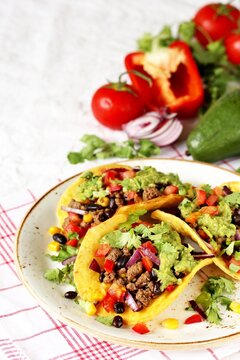 Mexican tacos with roast minced meat with corn and black beans, onions, fresh tomatoes, paprika and cilantro are flavored with guacamole sauce.