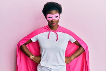 Young african american girl wearing super hero costume and medical mask relaxed with serious expression on face. simple and natural looking at the camera.