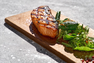 Macro shot of grilled salmon steak with bbq, fresh greens. Barbecue red trout fish fillet decorated with spicy greens on restaurant
