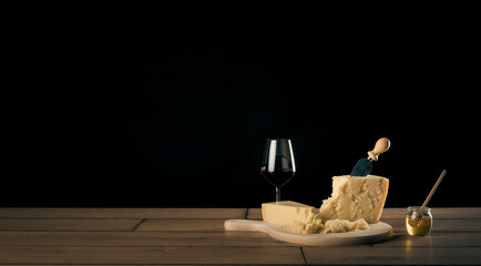 Tavola imbandita con due bicchieri di vino rosso, formaggio parmigiano reggiano su un tagliere con coltello e miele in un contenitore di vetro con dosatore.