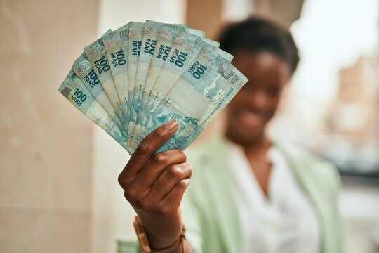 Young african american businesswoman smiling happy holding brazilian real banknotes at the city