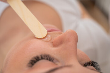 The master applies the anesthetic gel with a spatula to the woman's face before laser depilation. Mustache removal