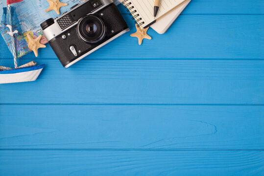 Overhead photo of camera map starfish ship notepad and pen isolated on the blue wooden background with copyspace