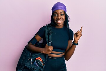 Young african american woman holding gym bag smiling happy pointing with hand and finger to the side