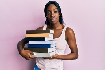 Young african american woman holding books relaxed with serious expression on face. simple and natural looking at the camera.