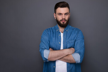 Confident serious hipster modern bearded man in jeans shirt with crossed arms is posing and looking...