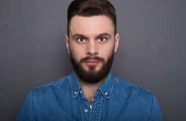 Close up portrait of confident serious bearded modern man while he looks on the camera