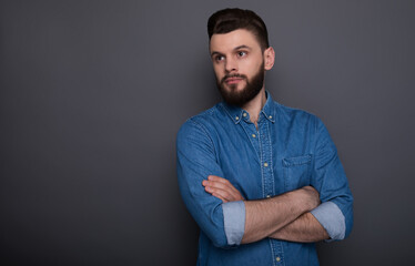 Confident serious hipster modern bearded man in jeans shirt with crossed arms is posing and looking right on the camera.