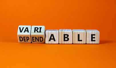 Dependable or variable symbol. Turned wooden cubes and changed the word dependable to variable. Beautiful orange background, copy space. Business and dependable or variable concept.