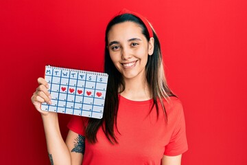 Young hispanic woman holding heart calendar looking positive and happy standing and smiling with a confident smile showing teeth