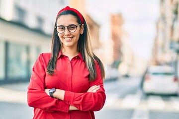 Young hispanic woman with arms crossed smiling happy at the city.