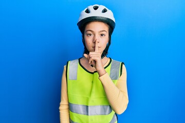 Beautiful brunette little girl wearing bike helmet and reflective vest asking to be quiet with finger on lips. silence and secret concept.