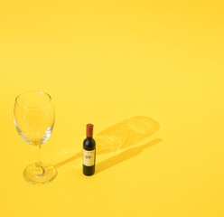 Wine glass standing near mini botle of red wine.Yellow background.