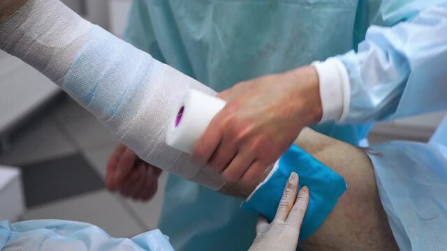 Close-up of the hand of a phlebologist applies a gauze bandage to the patient's leg after the procedure. Treatment of varicose veins. Nurse with gloves holding a bandage on the wound
