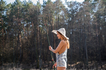 A girl stands on the shore of a forest lake and catches fish with a fishing rod.