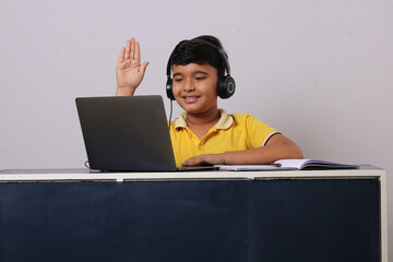 Happy indian school pupil or boy wearing headphones raising hand distance learning online at virtual lesson class