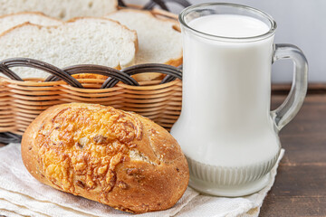 freshly baked diet bun, a mug of milk and bread in a basket on a wooden table