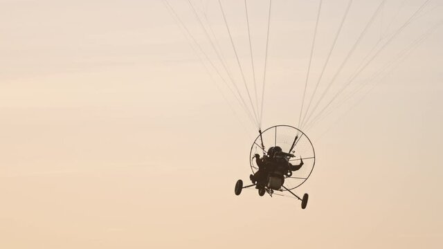 Close-up of paramotor seat hanged under parachute flying away against sunset sky. Tandem motor powered paragliding at twilight. 