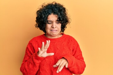 Young hispanic woman with curly hair wearing casual winter sweater disgusted expression, displeased...