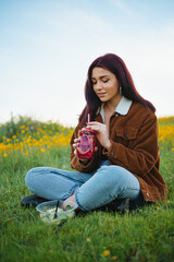 Teenager girl drinking water in a red jar sitting on the grass of a hill. She has a salad next to her.