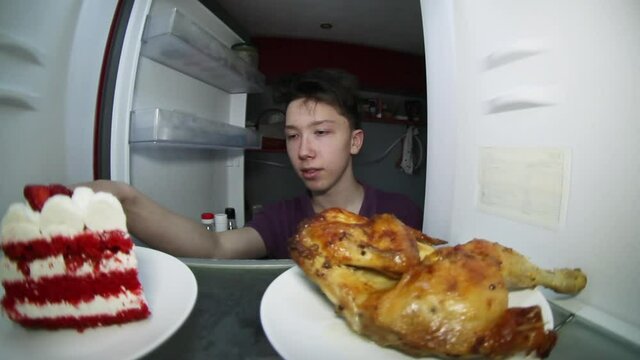 A teenager searches the refrigerator for food. Makes a choice: smoked chicken or a piece of cake .