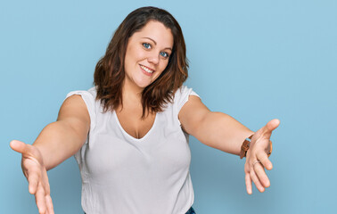 Fototapeta premium Young plus size woman wearing casual white t shirt looking at the camera smiling with open arms for hug. cheerful expression embracing happiness.