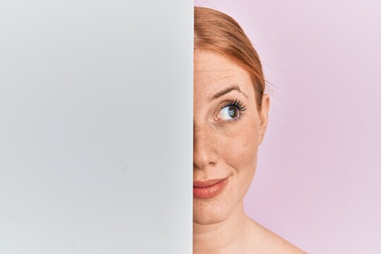 Young Irish Woman Holding Blank Empty Banner Showing Half Face Smiling Looking To The Side And Staring Away Thinking.