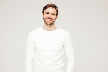 Portrait of handsome smiling hipster lumbersexual businessman model wearing casual white sweater and trousers. Fashion stylish man posing against gray background in studio